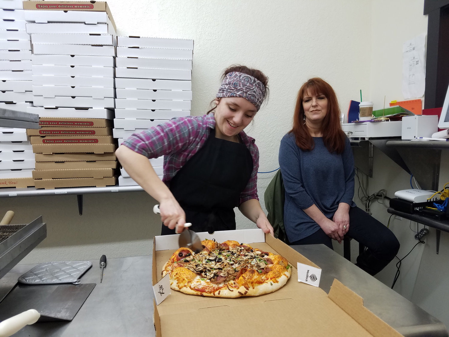 Kaitlyn Bornstein cuts a completed pizza while business owner Kay Merino looks on at Maverick's Pizza in Centralia. The pizza shop offers dine-in, take-out and bake-at-home pizzas and hopes to soon offer delivery.