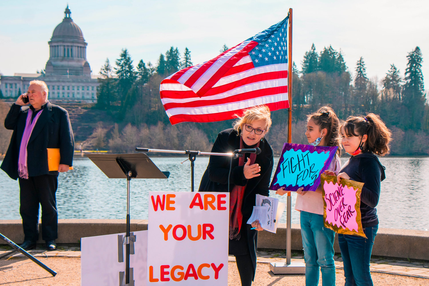 Kids hold signs as Michelle Darnell, President of the Ignite Foundation LLC, asks questions during a rally in support of bringing back in-person schooling near Capitol Lake on Saturday in Olympia.