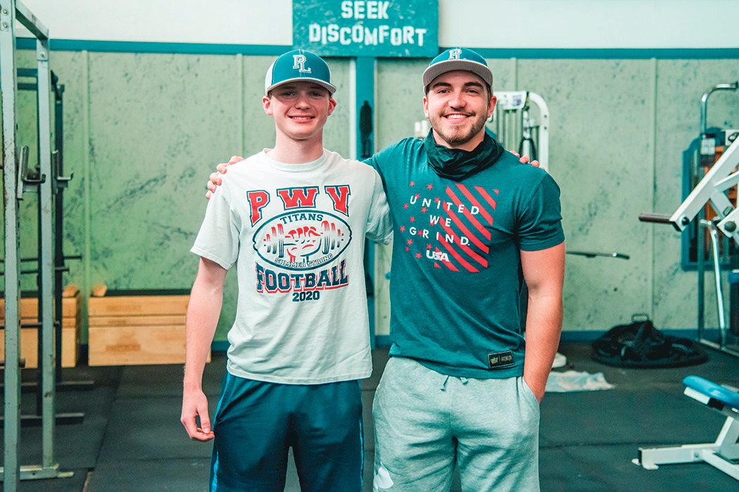 Joey McCalden and Kollin Jurek smile while posing for a photo in a weight room they designed and renovated at the Pe Ell school.