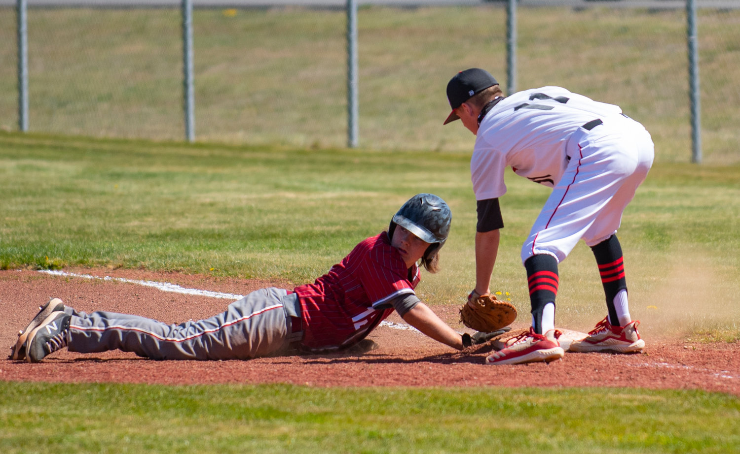 A Hoquiam runner slides safely back into first on a pickoff attempt by Tenino pitcher Easton Snider as Drew Hart (11) puts the tag on.