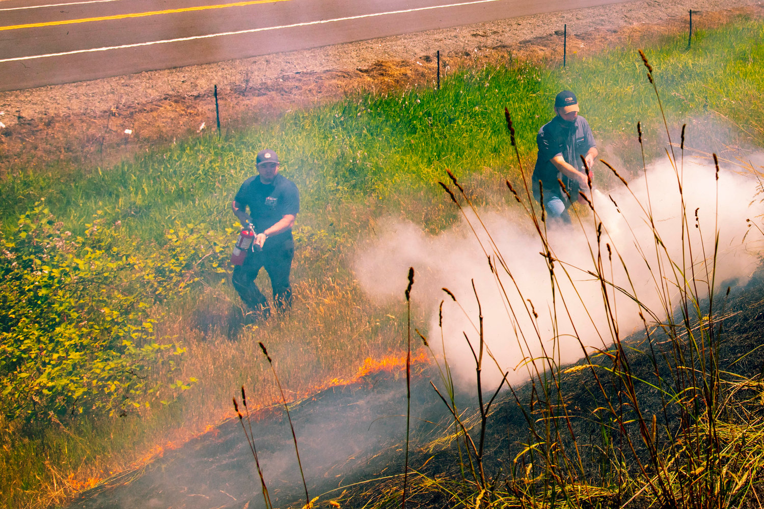 Employees from Awesome Ford and RV in Chehalis use fire extinguishers to put out a brush fire along the northbound lane of Interstate 5 on Tuesday.