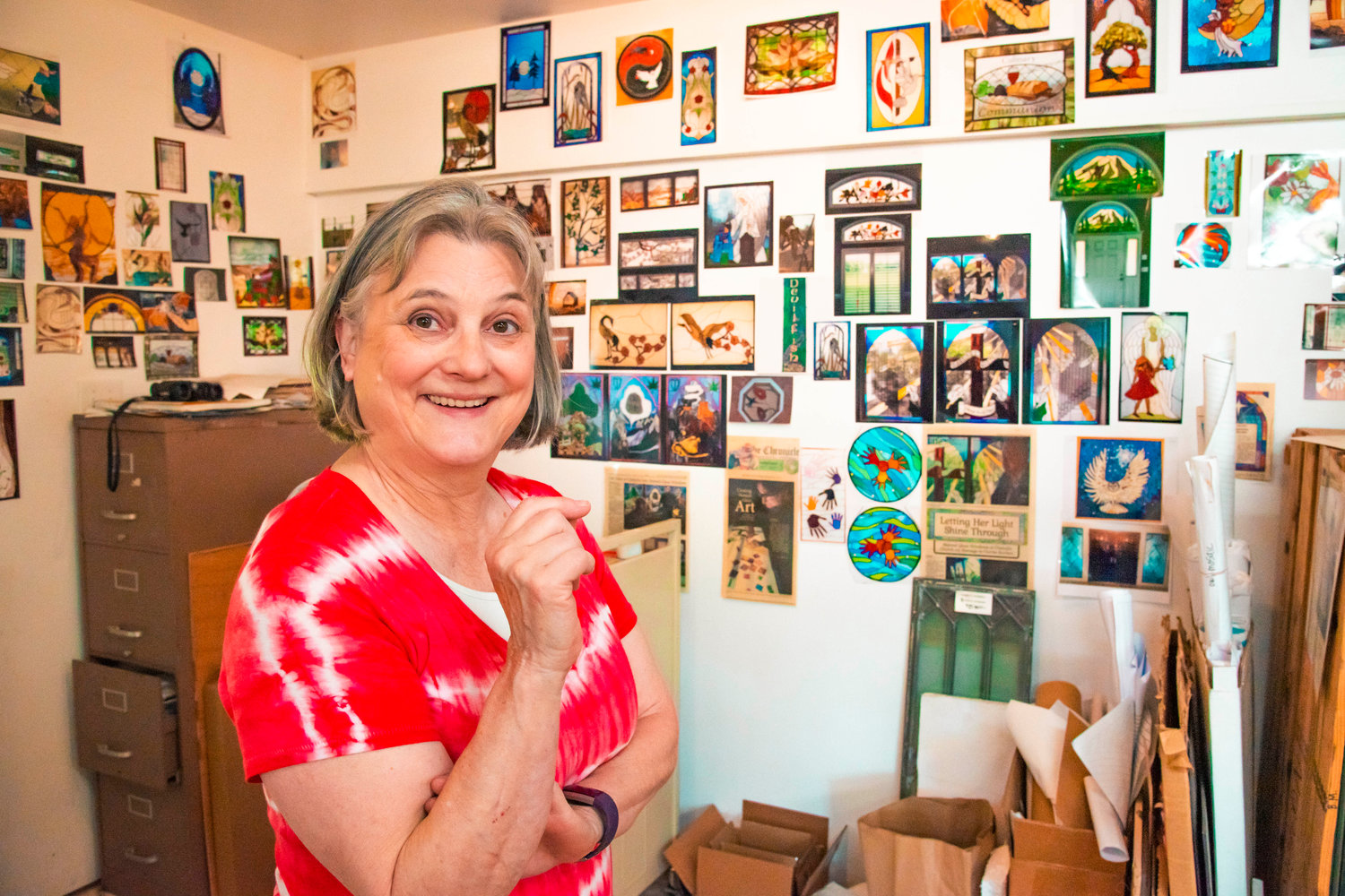 Marcy Anholt smiles while talking about stained glass artwork displayed in pictures around her studio.