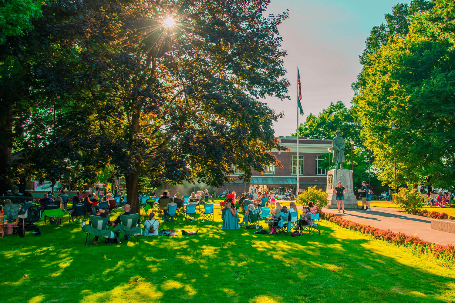 Sun shines through trees over George Washington Park in Centralia as community members gather during a “Music in the Park” event on Saturday.