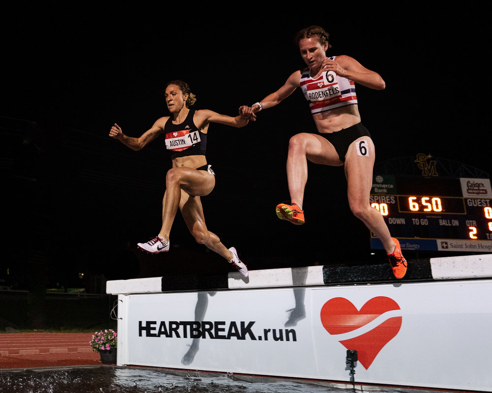 Caroline Austin, left, leaps over the steeplechase water pit at the Trials of Miles Kansas City Qualifier in May 2021.