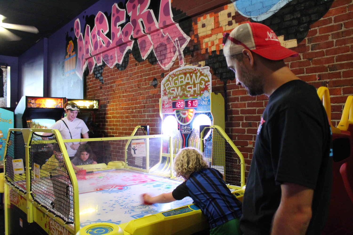 Ryan and Kim Brumbaugh, of Rochester, watch their kids Audrey, 7, Cybil, 5, and Niko, 3, play an air hockey style game from Japan called Big Bang Smash at Insert Coin in Centralia. Ryan Brumbaugh said he has become the retro arcade bar's "number one fanboy".
