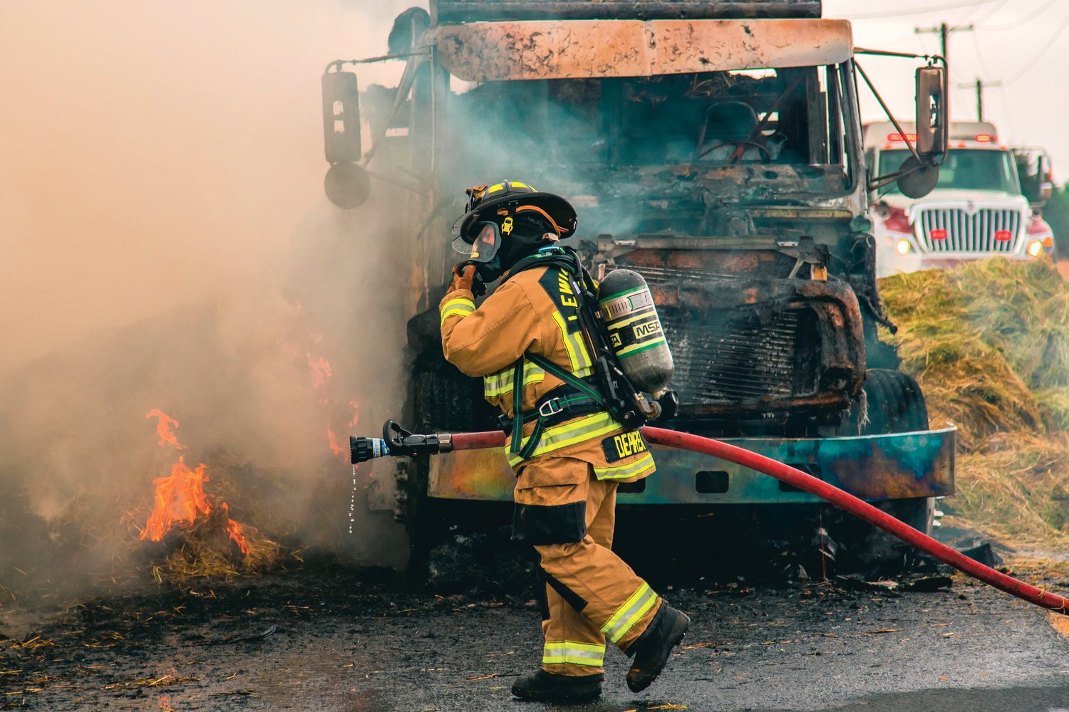 A firefighter adjusts his mask while responding to a hay truck fire on Highway 603 at the intersection of Tune Road west of Chehalis on Saturday.