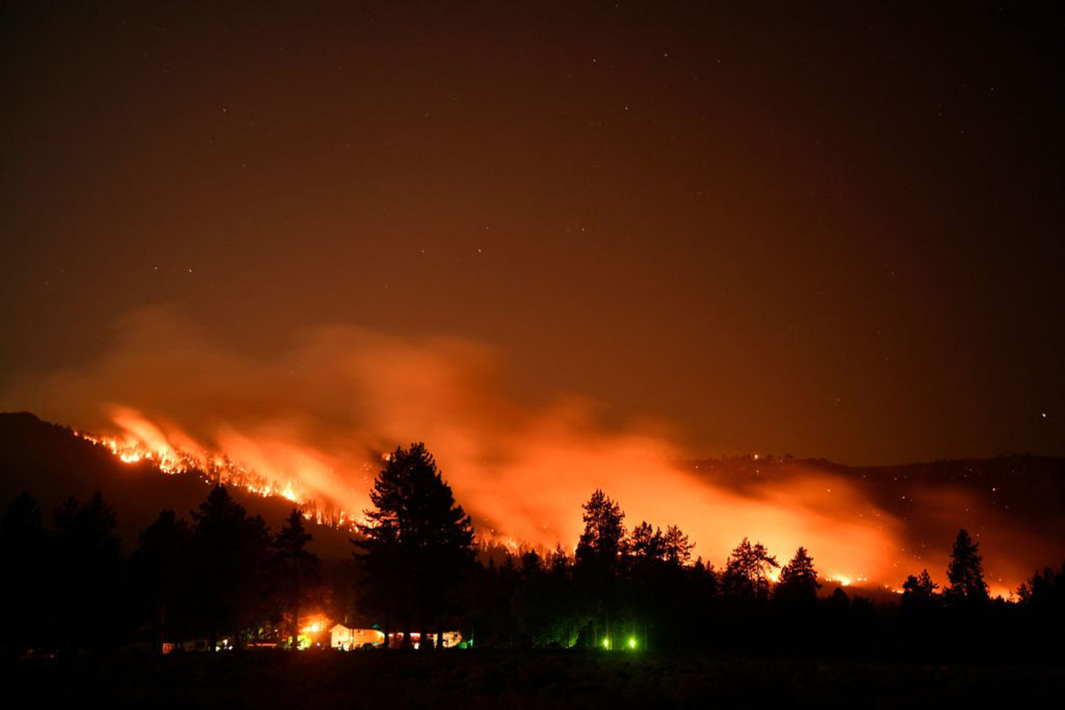 In this long exposure picture trees burn on a hillside behind Honey Lake campground during the Dixie Fire on August 18, 2021 in Milford, California. - The wildfire in Northern California continues to grow, burning over 626,000 acres according to CalFire. (Patrick T. Fallon/AFP via Getty Images/TNS)