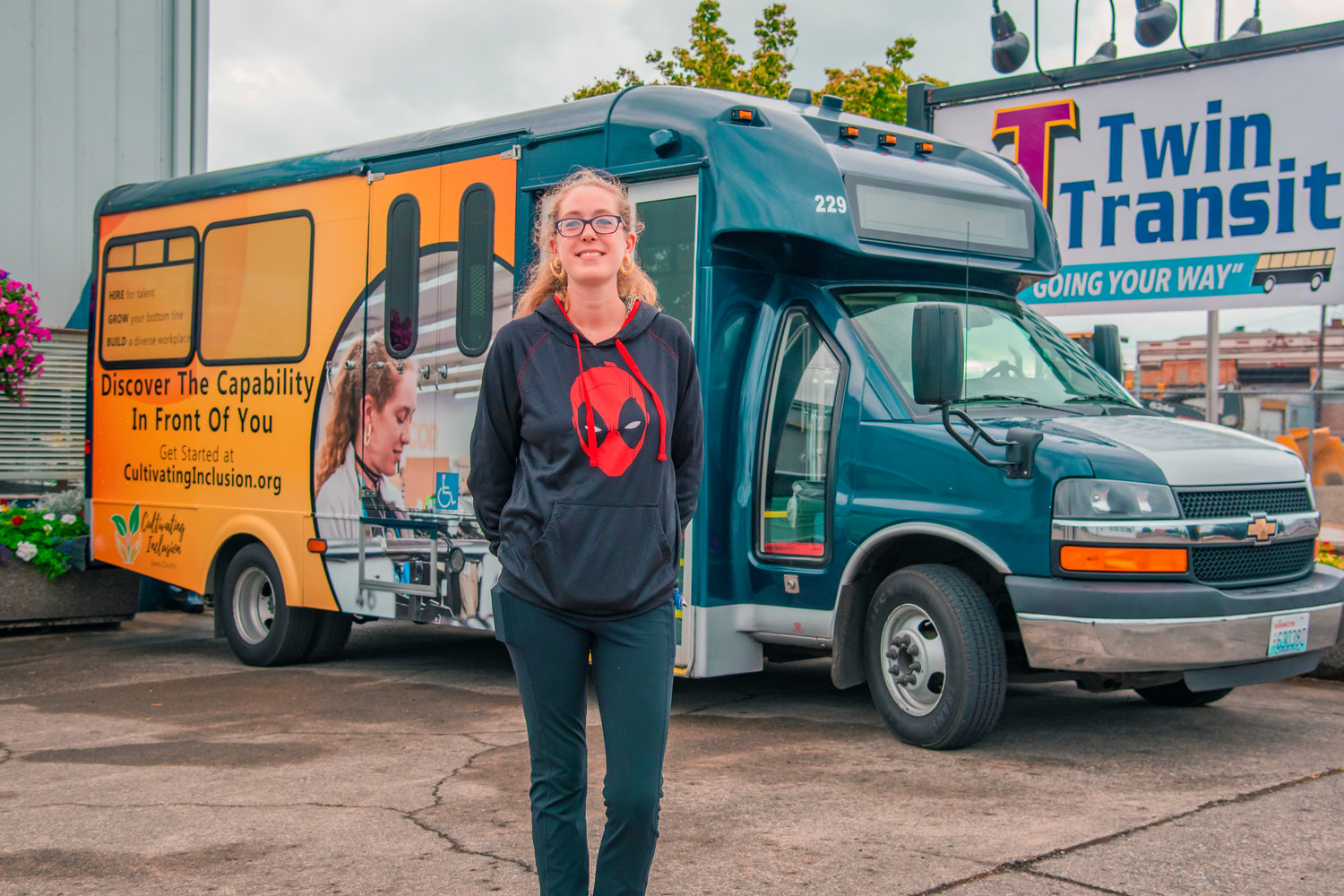 Hannah Byrd smiles and poses for a photo in front of newly wrapped Twin Transit ride featuring a photo of her working locally at Goodwill Thursday in Centralia during a Cultivating Inclusion job hiring campaign.