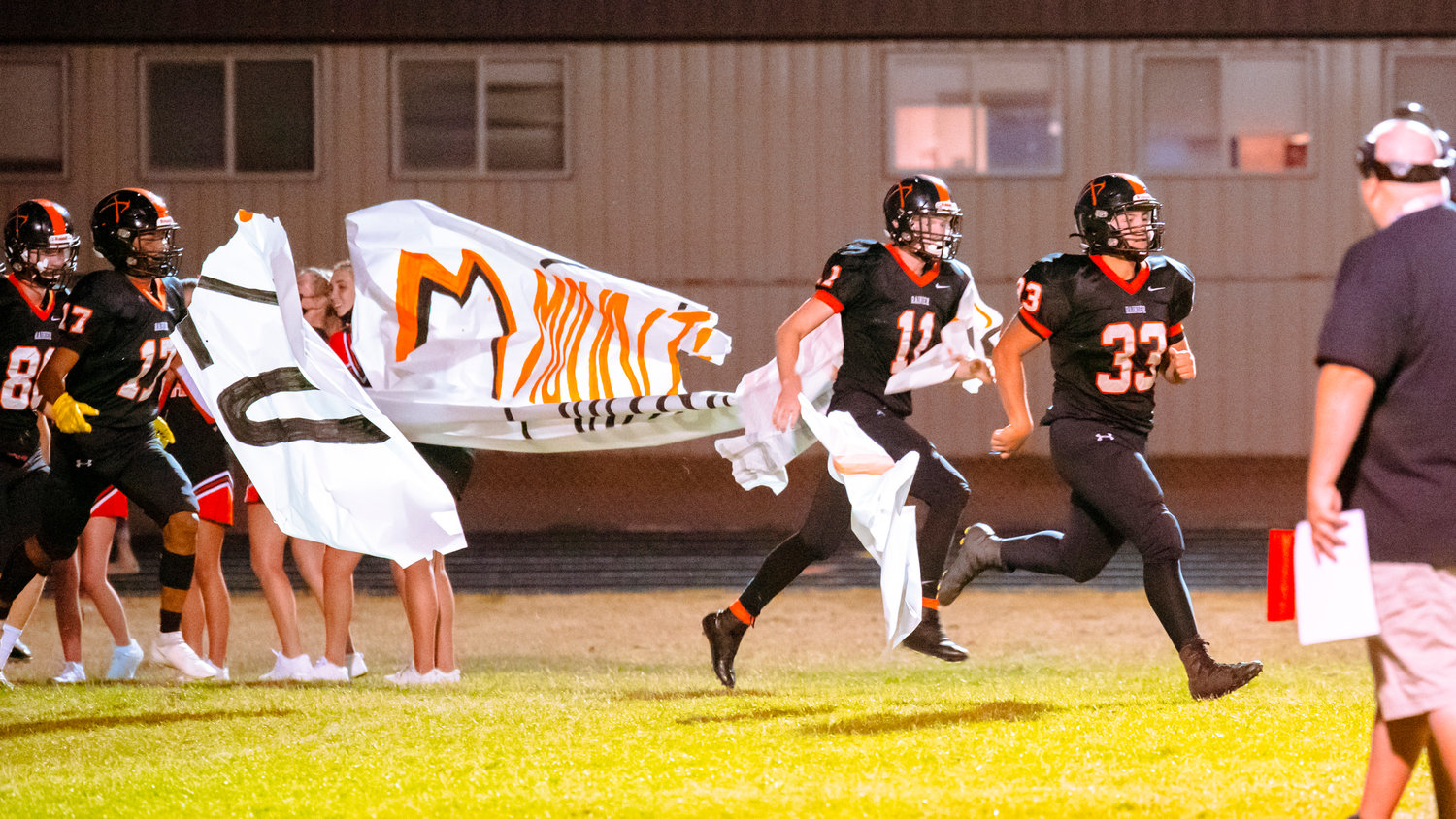 Rainier football players bust through a banner at halftime Friday night.