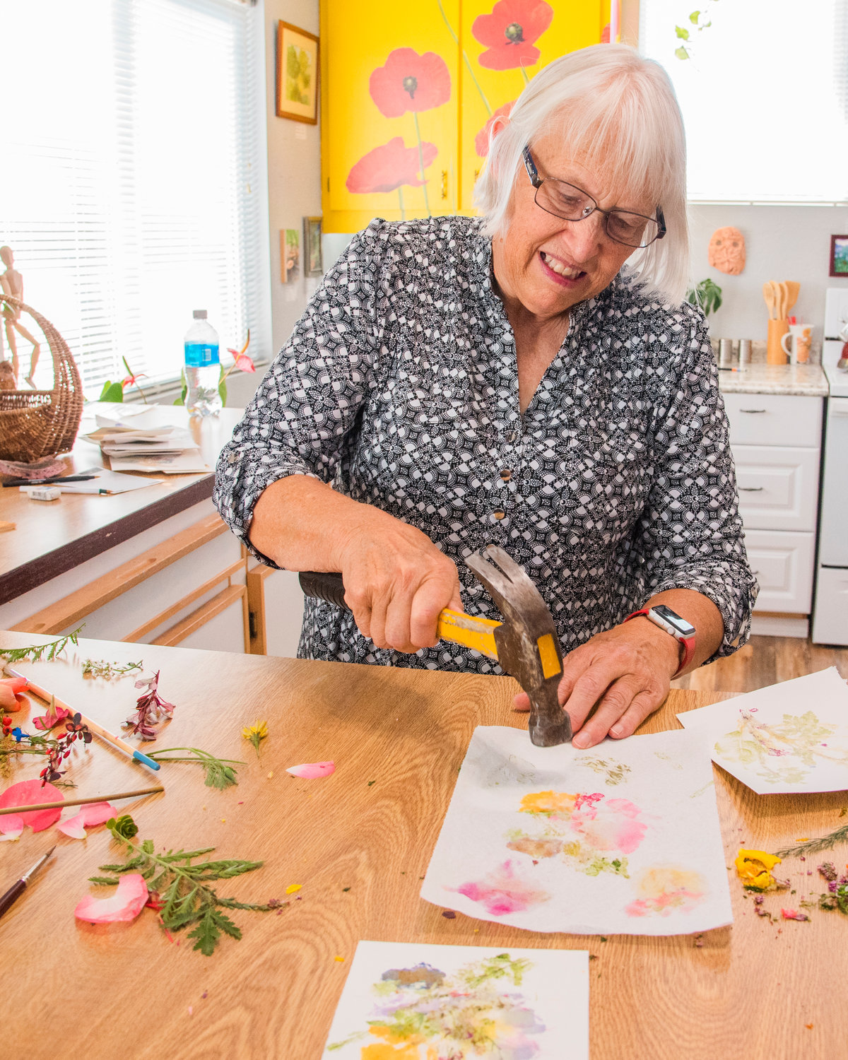 Barbara Burres pounds flowers against a table onto a canvas Tuesday afternoon in her Cinebar Art Studio.