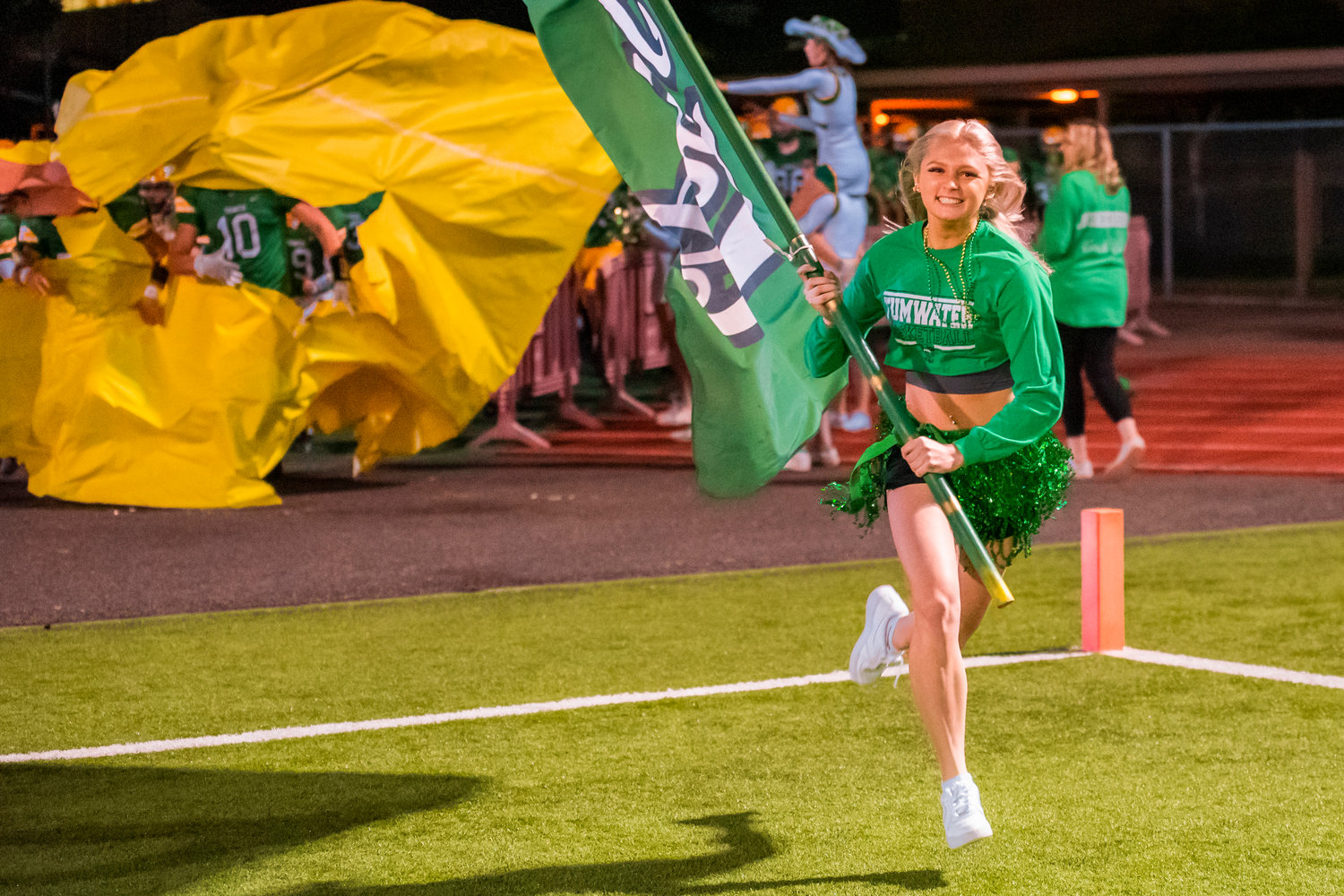 Avery Coker runs with the Tumwater flag as players bust through a paper enterance to the field at halftime Friday night.