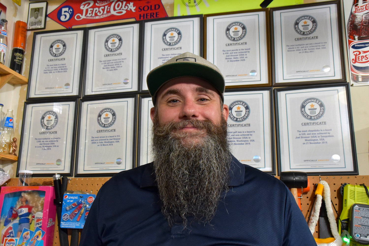 Joel Strasser smiles in front of his 10 world records for puting objects in his beard.