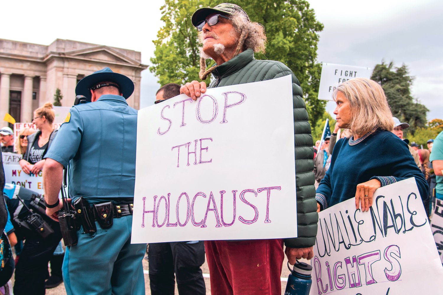A sign is held during a “Medical Freedom Rally” in Olympia that reads, “Stop The Holocaust,” as members of the Washington State Patrol respond to a medical event in the crowd Sunday afternoon.