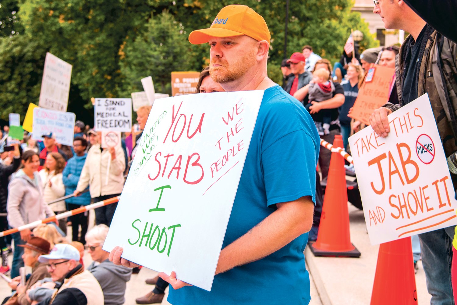 Stephen Hubbard holds a sign that reads, “You stab, I shoot,” along with the phrases, “United We Stand,” and “We The People,” during a “Medical Freedom Rally” outside the Washington State Capitol Building Sunday afternoon in Olympia.