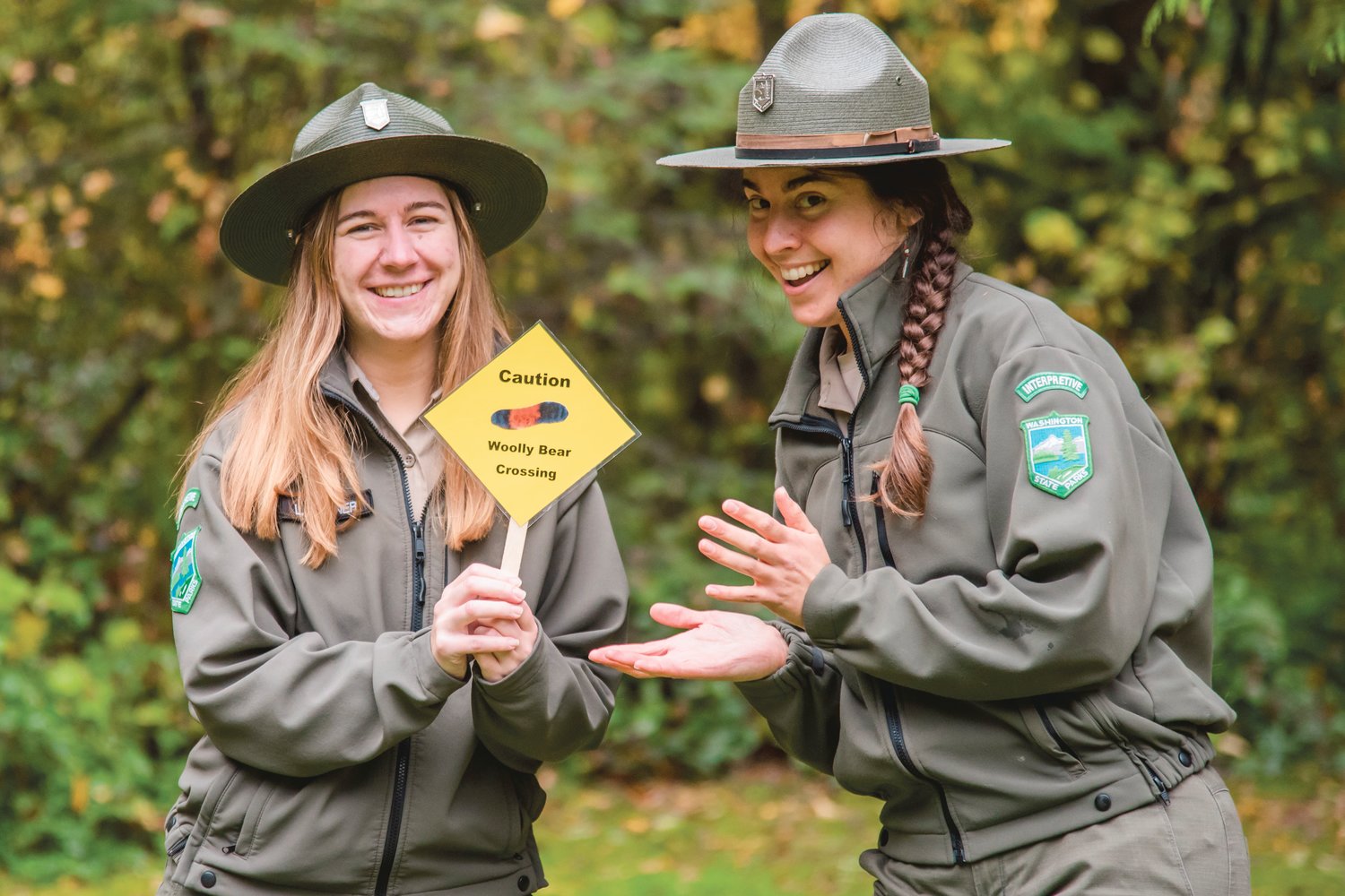 Leah Garner and Alysa Adams smile and pose for a photo with a sign that reads "Caution, Woolly Bear Crossing" at Lewis and Clark State Park Thursday morning.