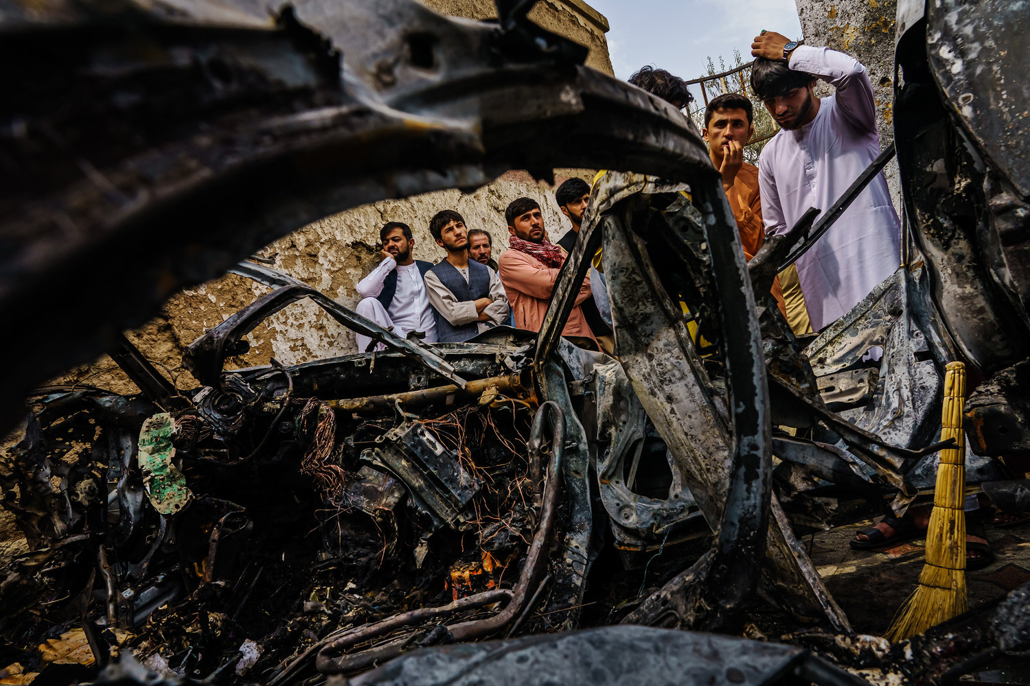 Relatives and neighbors of the Ahmadi family gathered around the incinerated husk of a vehicle that the family says was hit by a U.S. drone strike, in Kabul, Afghanistan, in August. (Marcus Yam/Los Angeles Times/TNS)