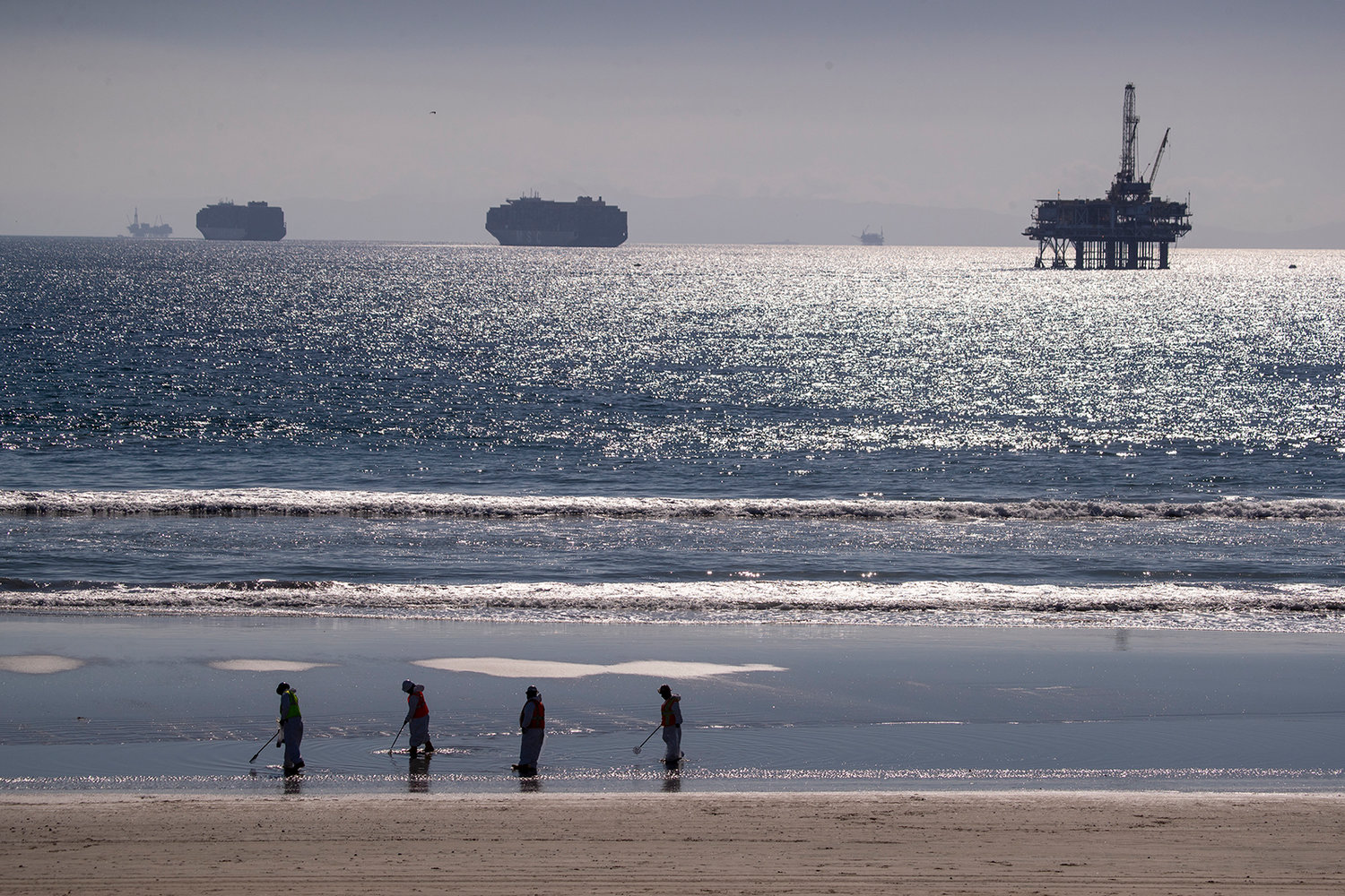 Container ships and an oil derrick line the horizon as environmental oil spill cleanup crews search the beach, cleaning up oil chucks from a major oil spill in Huntington Beach Tuesday, Oct. 5, 2021. (Allen J. Schaben/Los Angeles Times/TNS)