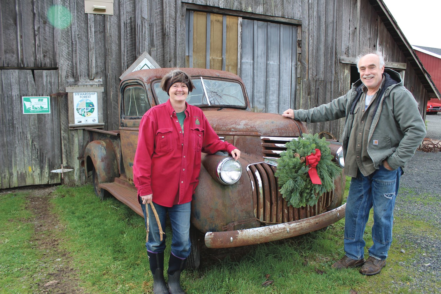 Karen and Eric Bernard, owners of Mistletoe Tree Farm near Winlock, stand near the old barn and pickup truck that greets visitors to the Christmas tree farm. The stewardship designation sign hanging on the barn is one of their prized possessions as the couple emphasizes caring for their land as part of their Christmas tree business.