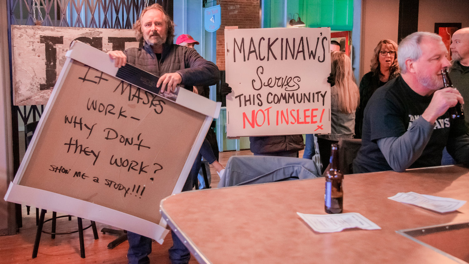 Supporters of Mackinaw’s display signs as members of the State Liquor Control Board remove alcohol from the premises Friday morning at Curious The Bar in Chehalis.