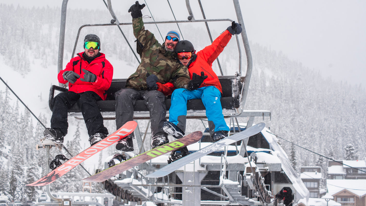 Snowboarders pose for a photo on opening day at White Pass while riding a lift.