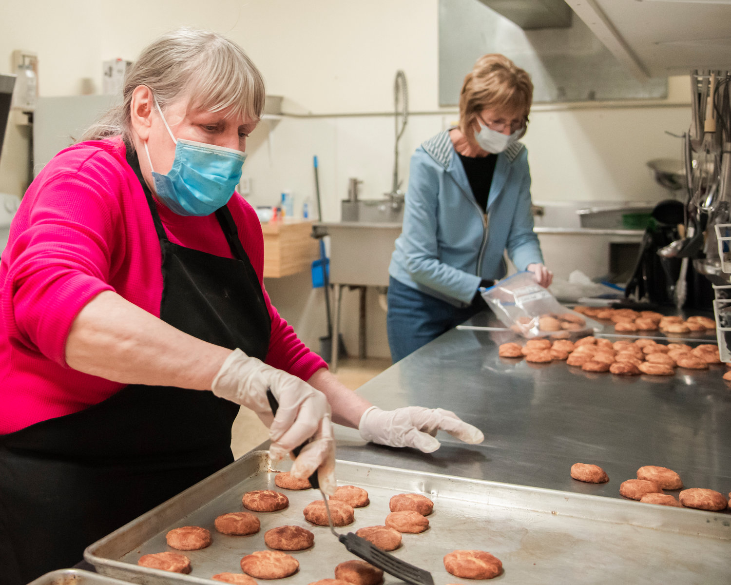 Judi Howard uses a spatula to remove snickerdoodle cookies from a pan before they are put into bags by Kay Klovdahl in preparation for Christmas meals at the Community Church of God in Centralia, Saturday morning.