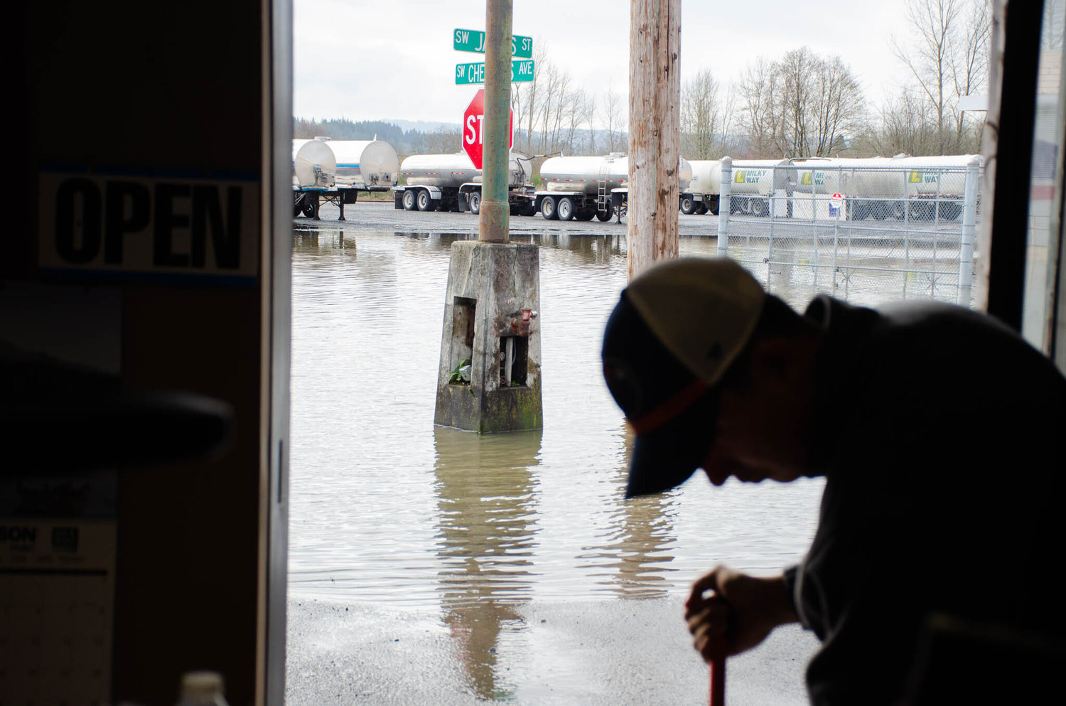 J.P. Padilla, a worker with Mills Northwest Heating and Cooling, squeegees flood water out from the business Saturday morning as flood water recede in the background.