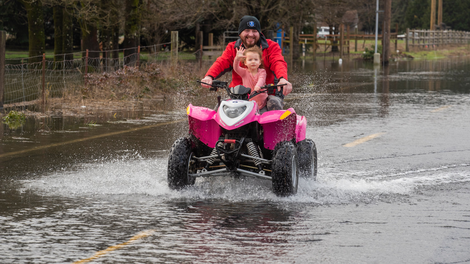 Mila Joy Watson, 3, waves while riding on her pink quad piloted by Nick Watson as he rides through flood waters to check on his brother along 183rd Avenue SW, in Rochester on Saturday.