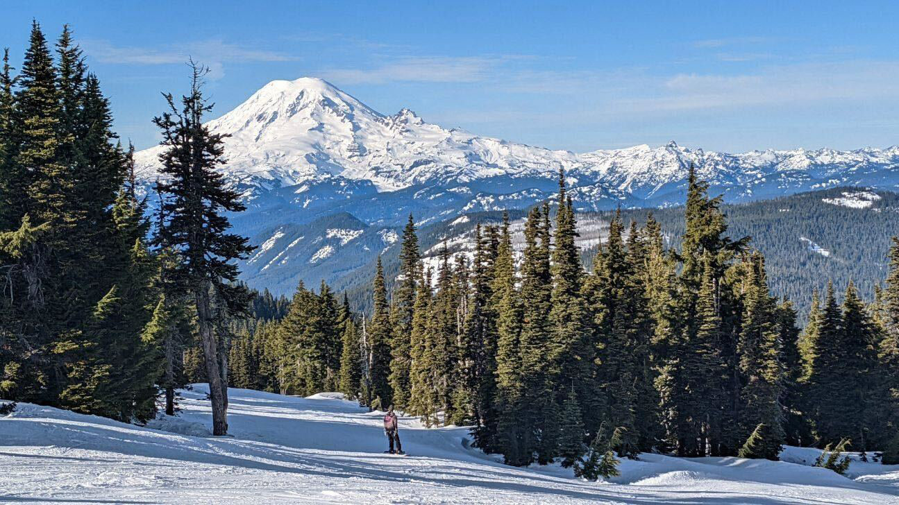 Mount Rainier stretches above foothills as a snowboarder rides down slopes in the White Pass Ski Area on Saturday.