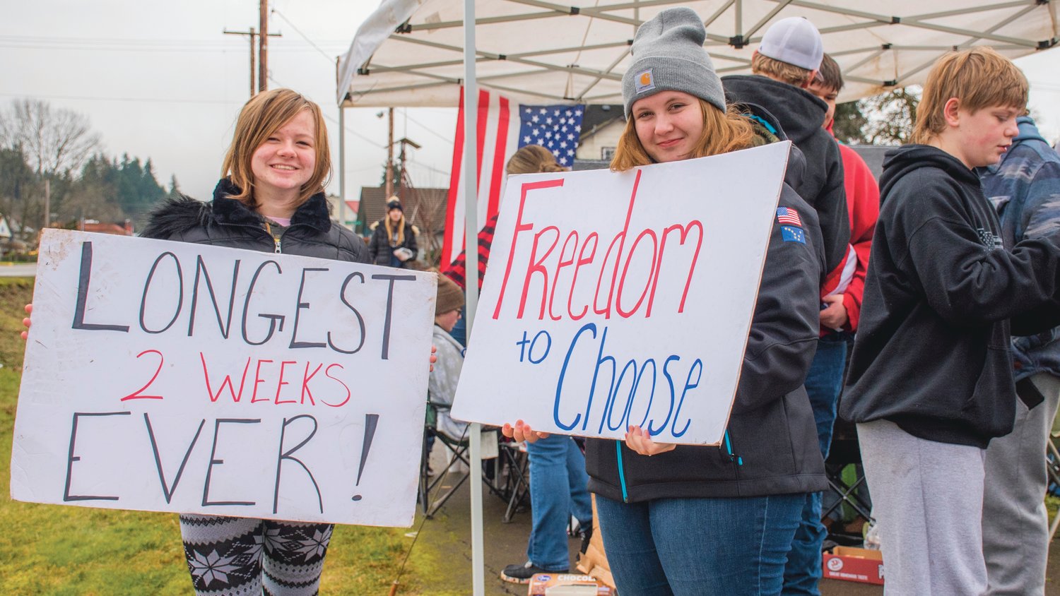 Randi Belanger, a 7th grader, and Kessa Smith, a sophomore, smile and hold signs during a demonstration outside the Pe Ell School District on Wednesday.
