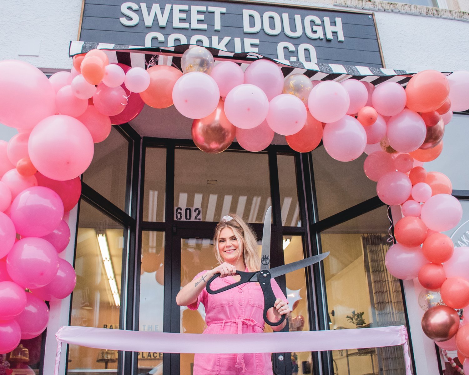 Ashlee Shirer, owner of Sweet Dough Cookie Co., smiles while holding a pair of scissors outside her Centralia storefront during a ribbon cutting ceremony Saturday morning.