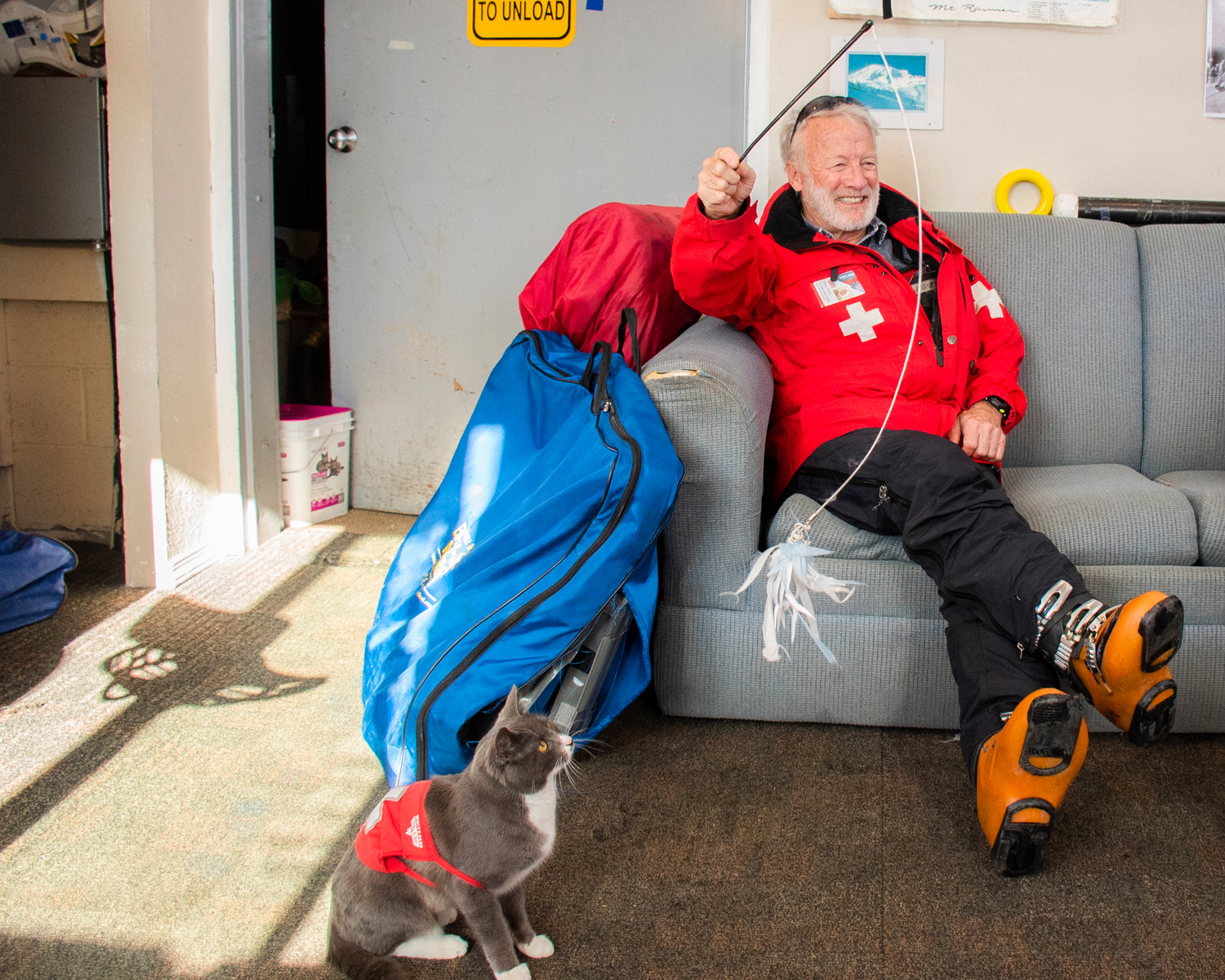 Michael “Murph” Murphy smiles while holding a cat toy as Uzi looks on inside patrol dispatch at the top of the Great White Express chairlift on Sunday.