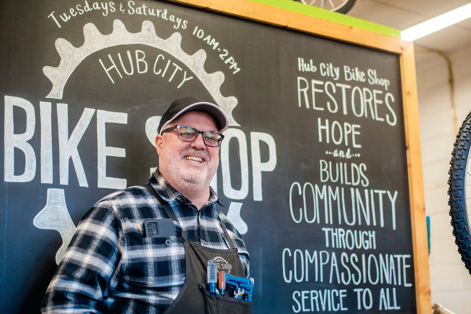 Dave Smith smiles for a photo in front of a chalk board on display inside the Hub City Bike Shop in Centralia.