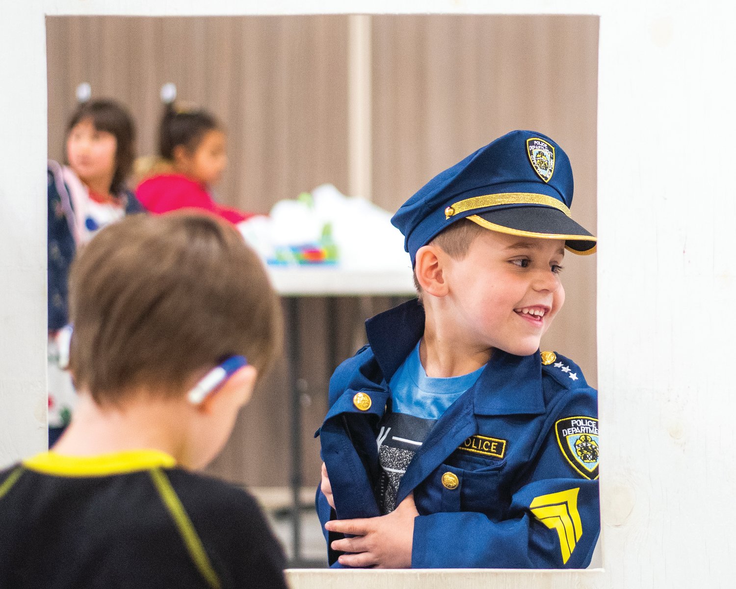 Chase Lovato smiles and sports a police uniform as fellow kindergarten students take on roles in Scooter Town Tuesday morning.