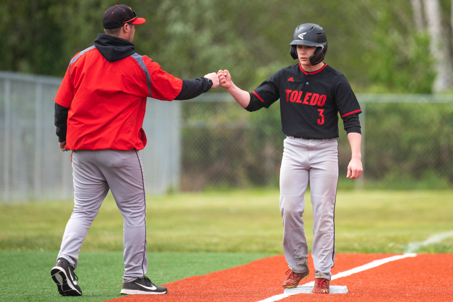 Toledo coach Mack Gaul, left, fist-bumps Toledo's Justin Filla on third base during a district-playoff win over Ilwaco on May 7.