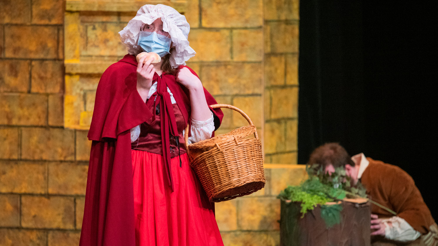 Emily Cole holds bread up to a mask while playing Little Red Riding Hood during dress rehearsals for “Into The Woods,” presented by the Centralia College Theatre program.