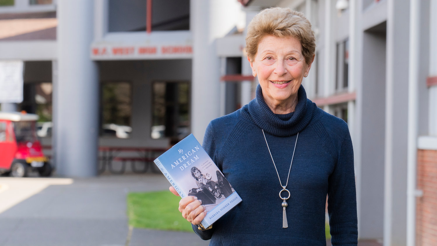 Barbara Sommer Feigin smiles for a photo with her book “My American Dream” while standing outside W.F. West High School  in Chehalis.