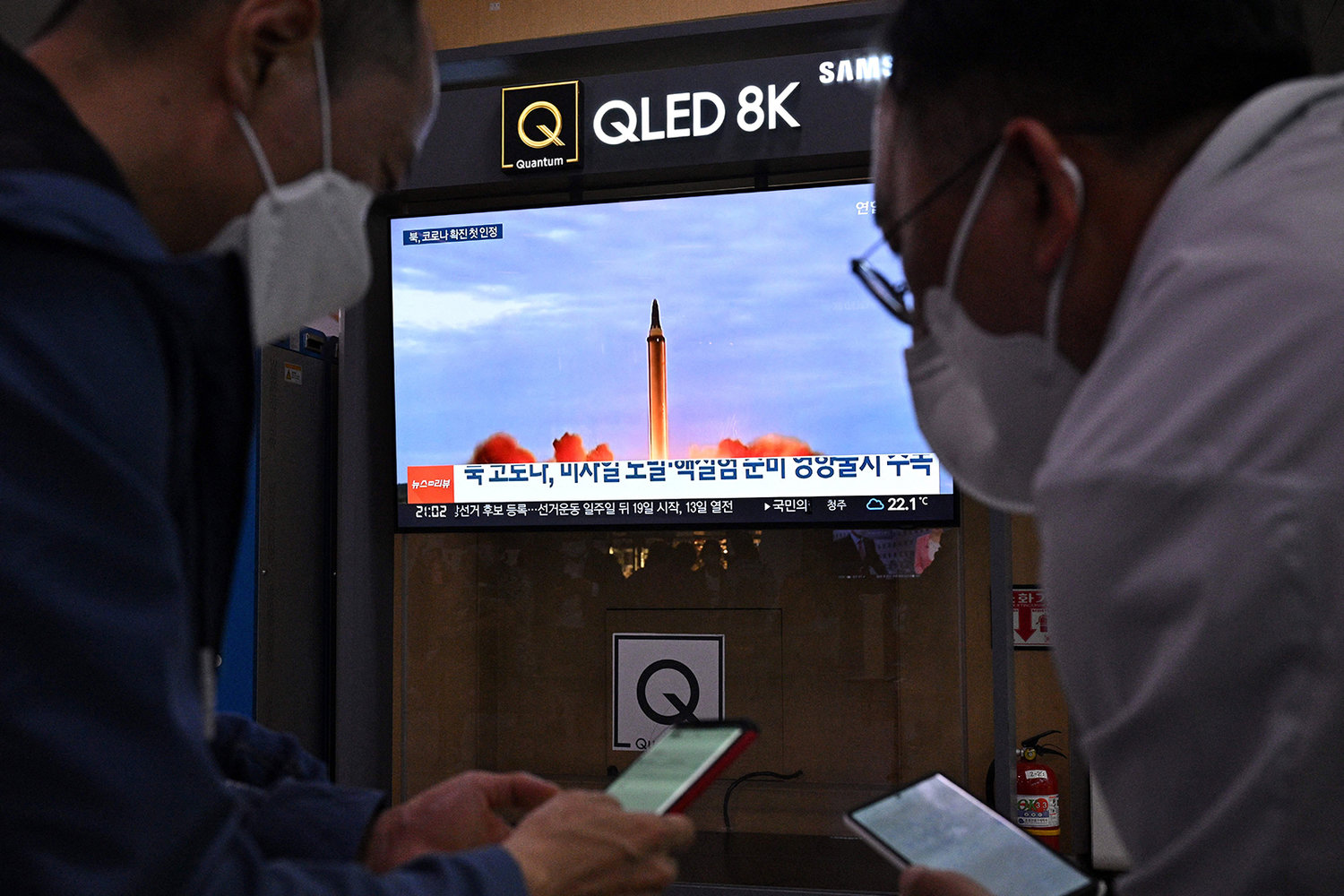 Two men check their phones as a television screen shows file footage of a North Korean missile test during a news broadcast in Seoul on May 12, 2022, after Seoul's military said it had detected three short-range ballistic missiles fired from near Pyongyang. (Anthony Wallace/AFP via Getty Images/TNS)