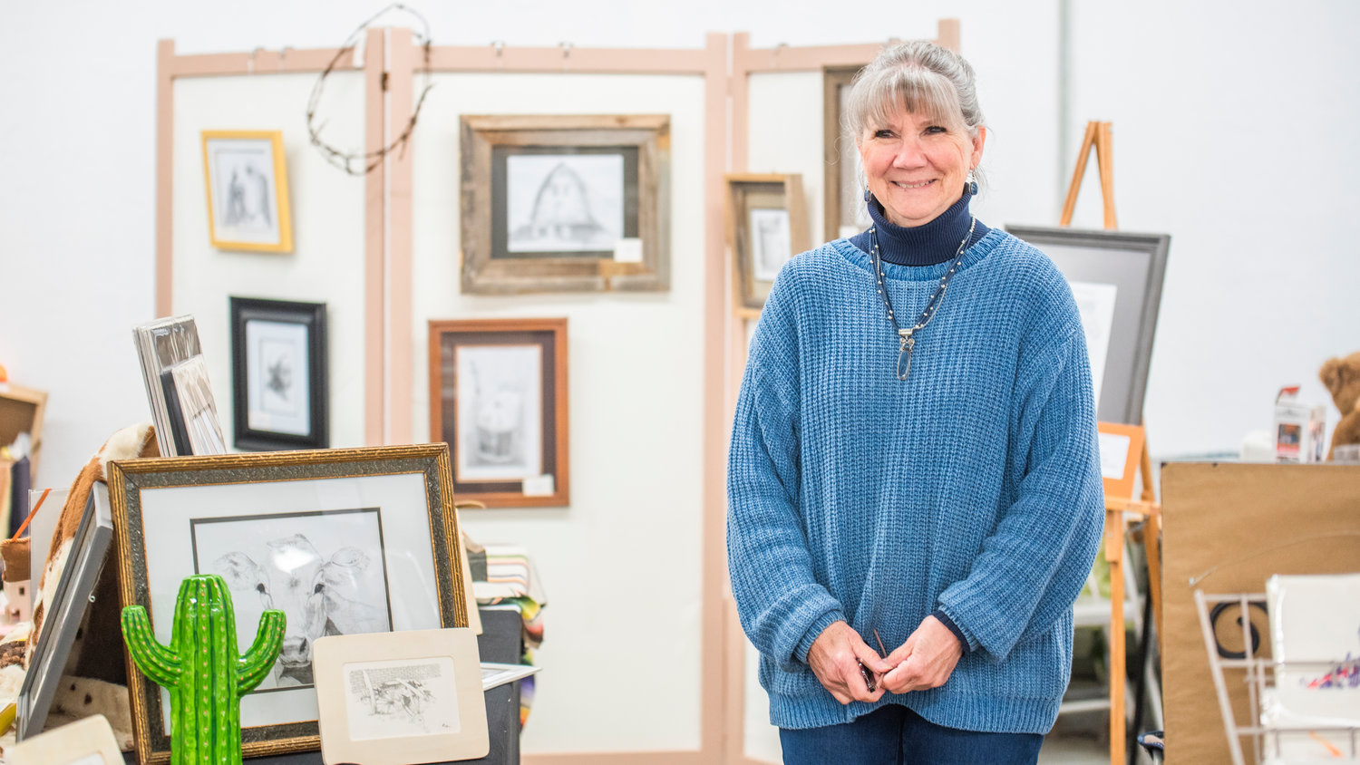 Pat Anderson smiles while standing next to her art on display at the Southwest Washington Fairgrounds in Centralia on Saturday during the Spring Community Garage Sale.