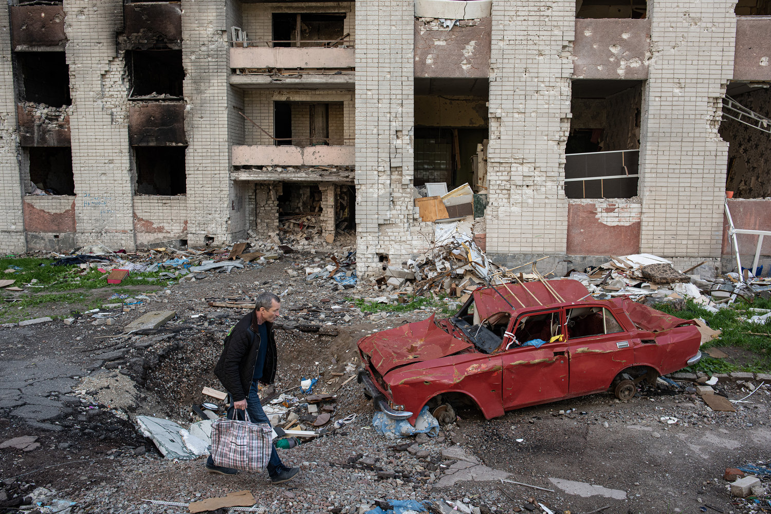 A man carries his belongings past a destroyed car next to a heavily damaged apartment building on May 28, 2022, in Chernihiv, Ukraine. (Alexey Furman/Getty Images/TNS)