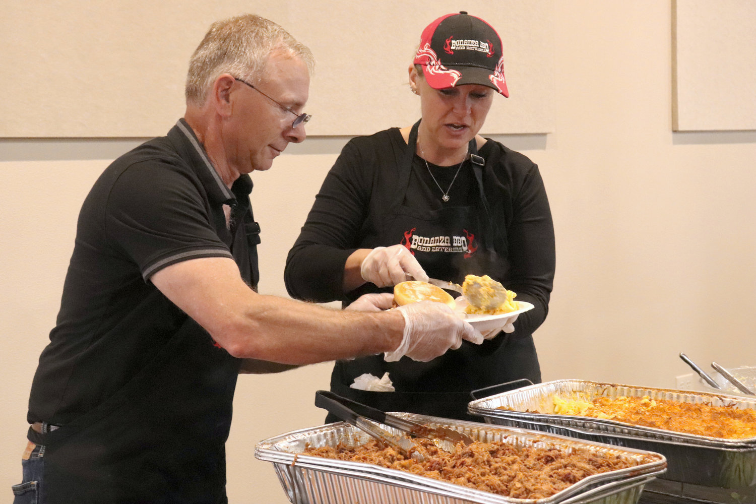 Chris Gorton and Evie Degravelles of Bonanza BBQ & Catering dish up a plate of food during the Rob Fuller Top 25 Scholarship Luncheon in Chehalis in Monday.