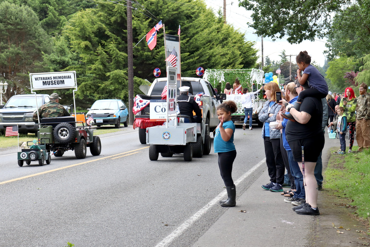 People wave as small vehicles representing the Veterans Memorial Museum pass by during the Swede Day Parade in Rochester on Saturday.