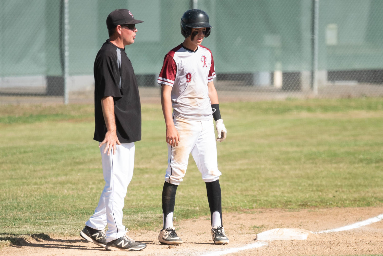 I-5 Jeep Renegades infielder Cal Bullock is counseled by his father and coach, Bryan, on the basepath against the Tenino Trappers July 15 in Chehalis.