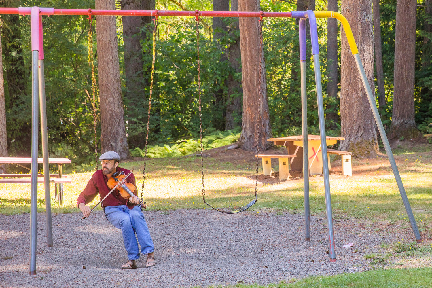 Steve Cox sits on a swing while playing a violin at Winolequa Memorial Park in Winlock Saturday morning.