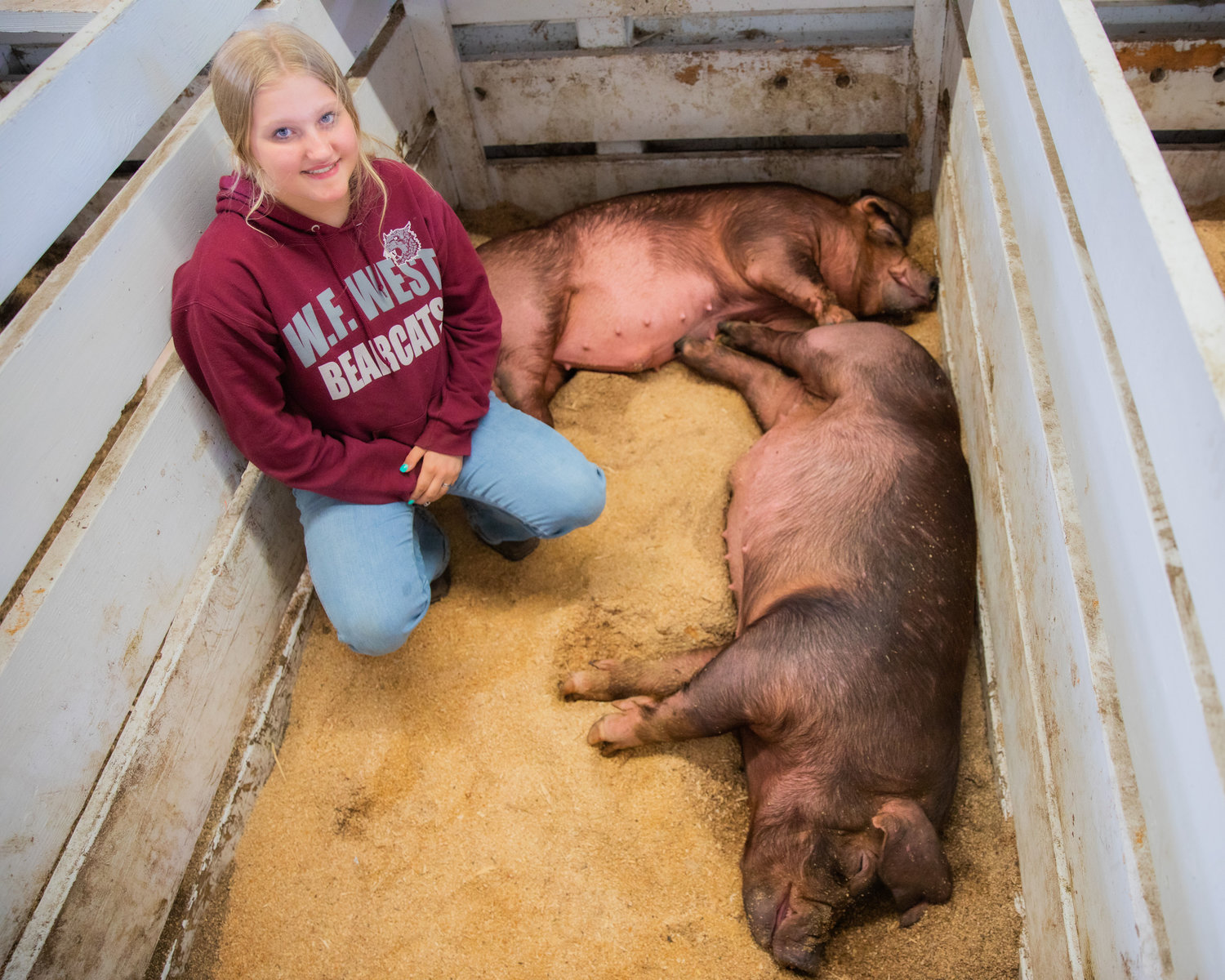 Logan Nailoon, 13, smiles for a photo alongside pigs in a pen Monday afternoon at the Southwest Washington Fairgrounds in Centralia.