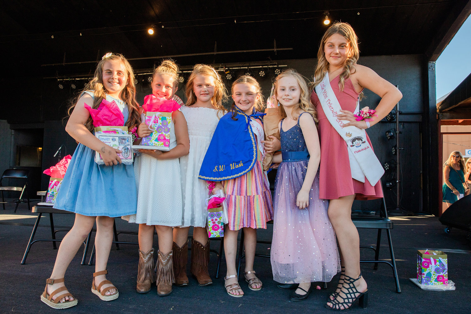 Little Miss Friendly candidates Jaxsyn Lowrey, Ella Hughes, Finley Swope and Gracelyn Briggs smile for a photo with Emma Britton, sporting the iconic cape, on the Saloon Stage at the Southwest Washington Fairgrounds in Centralia on Tuesday. Former Little Miss Friendly MaKayla Maynard is pictured far right.