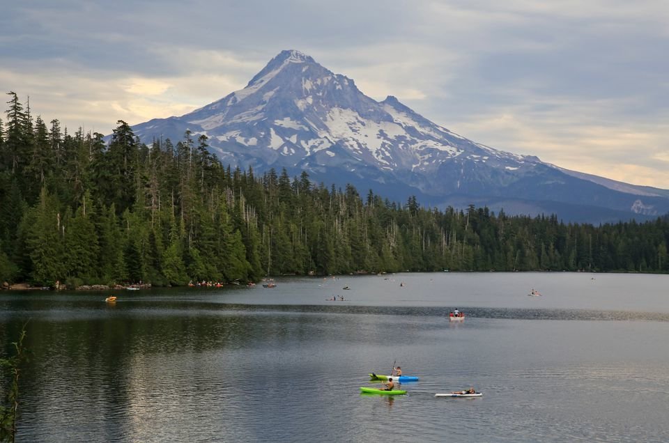 Kayaks, rowboats and paddle boards take to Lost Lake on a cloudy summer day, with Mount Hood in the near distance.