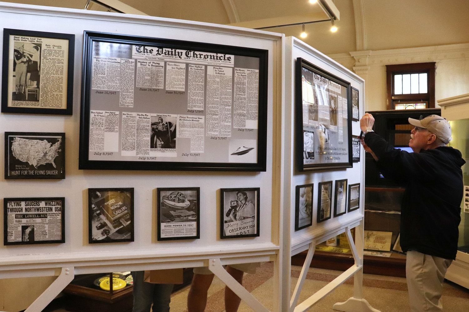 A Lewis County Historical Museum attendee takes photos of old Chronicle articles on display as part of a UFO exhibit during the Chehalis Flying Saucer Party on Saturday.