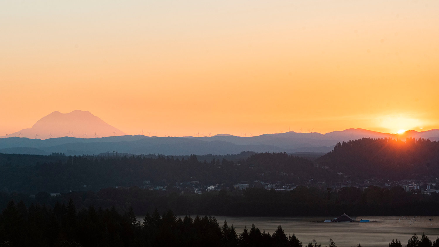 The sun rises Tuesday morning in this photograph captured from a hill west of Chehalis. Mount Rainier is pictured at left with wind turbines from the Skookumchuck Wind Project visible on the ridge
