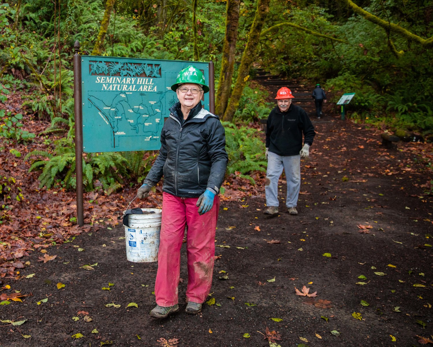 Ginger Sarver smiles while carrying a bucket and helping with trail work at the Seminary Hill Natural Area in Centralia on Wednesday.