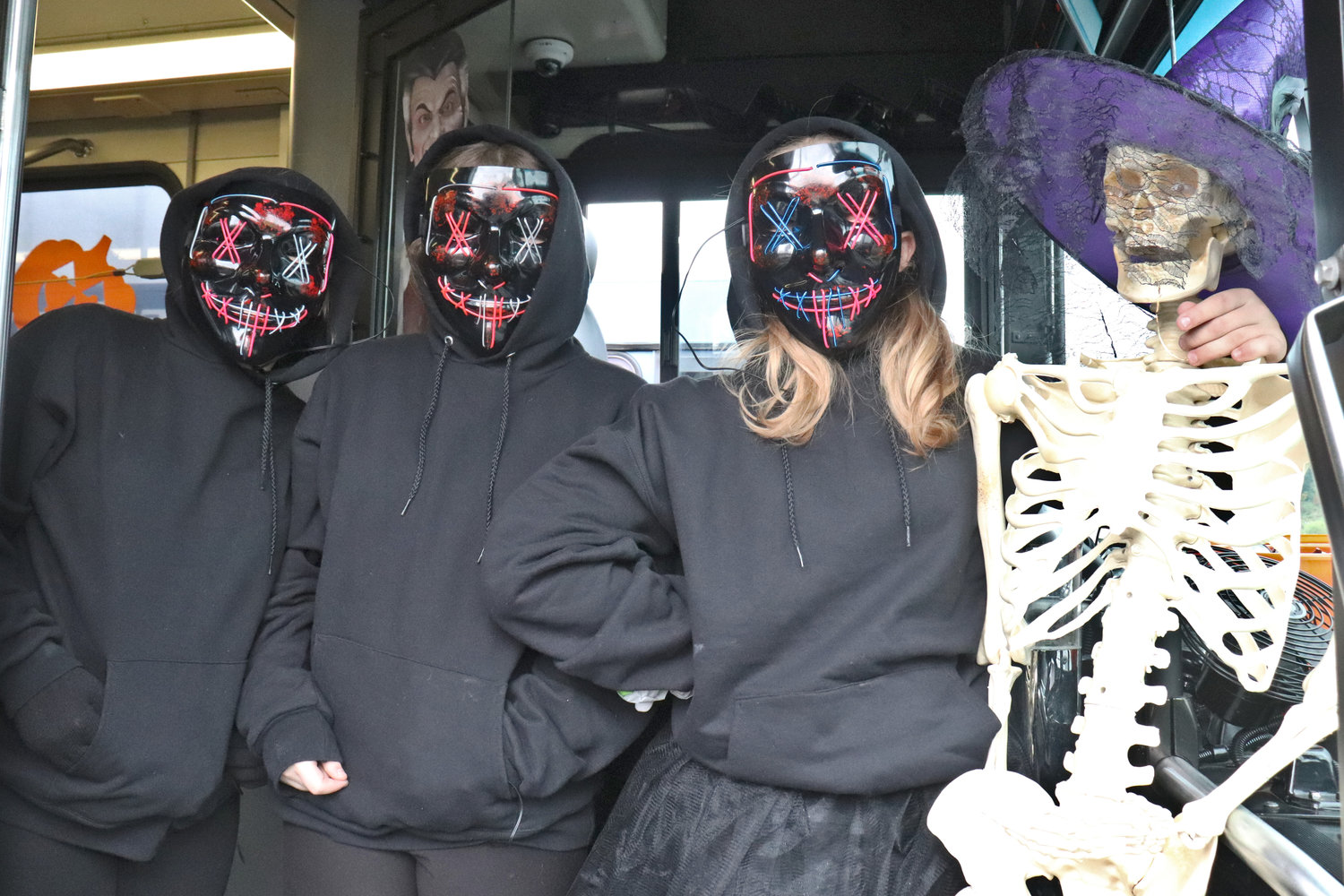 Nicole Freeman, Destiny Ingram and Sisylia Bowen pose for a photo with a skeletal passenger on one of the buses Twin Transit decorated for Trick or Treat Transit.